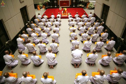 นาคธรรมทายาทในชุดขาวนั่งพนมมือเรียงแถวในพิธีบรรพชาอุปสมบทหมู่