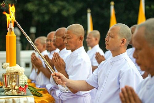 นาคธรรมทายาทชายหลายคนในชุดขาวกำลังถืออุปกรณ์จุดเทียนด้วยความสำรวมในพิธีบรรพชาอุปสมบทหมู่