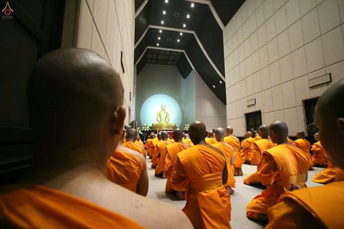 กลุ่มพระภิกษุและสามเณรนั่งพนมมือประกอบศาสนกิจภายในพระอุโบสถที่มีพระพุทธรูปประดิษฐานอยู่ด้านหน้า
