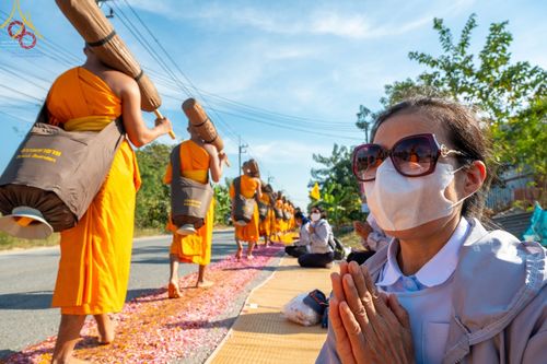 พุทธศาสนิกชนนั่งพนมมือต้อนรับคณะพระธรรมยาตราที่เดินธุดงค์บนเส้นทางโรยกลีบดอกไม้