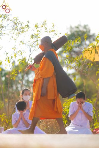 พระภิกษุเดินธุดงค์ท่ามกลางพุทธศาสนิกชนที่นั่งพนมมือแสดงความเคารพ