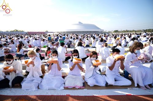 พุทธศาสนิกชนในชุดขาวถือถุงดอกดาวเรืองร่วมพิธีต้อนรับพระธรรมยาตรา ณ อนุสรณ์สถานบางปลา