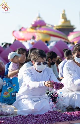 พุทธศาสนิกชนสวมชุดขาวกำลังโปรยกลีบดอกไม้ต้อนรับพระธรรมยาตราในพิธีทางศาสนา ณ อนุสรณ์สถานบางปลา