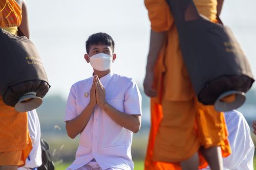ชายสวมชุดขาวพนมมือต้อนรับคณะพระธรรมยาตราที่เดินผ่าน ณ วัดบางปลา