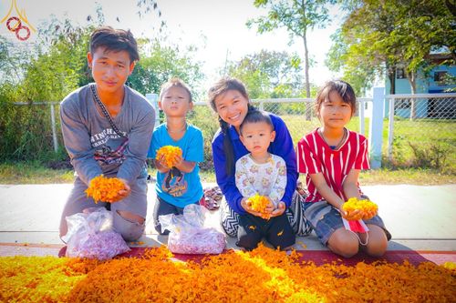 กลุ่มครอบครัวและเด็กๆ นั่งถือกลีบดอกดาวเรืองสีเหลืองเพื่อเตรียมโปรยต้อนรับพระธรรมยาตรา
