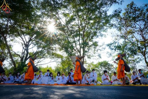 พระธรรมยาตราเดินผ่านพุทธศาสนิกชนชุดขาวที่นั่งรอรับด้วยความศรัทธาในยามเช้า