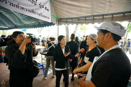 ผู้สื่อข่าวกำลังสัมภาษณ์จิตอาสาที่จุดบริการอาหารและน้ำดื่ม โดยมีช่างภาพบันทึกวิดีโออยู่ด้านข้าง
