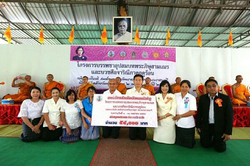 กลุ่มบุคคลยืนถือป้ายโครงการบรรพชาอุปสมบทพระภิกษุสามเณรและบวชศีลจาริณีภาคฤดูร้อน พร้อมพระภิกษุสงฆ์นั่งอยู่ด้านหลัง