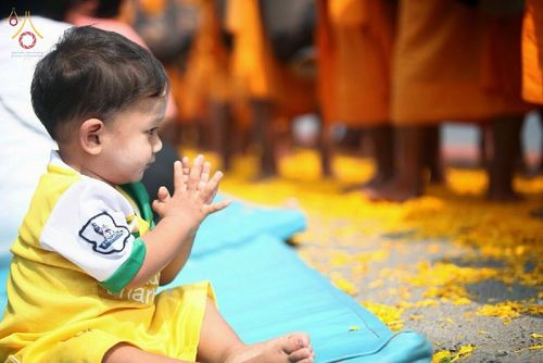 เด็กชายตัวน้อยนั่งพนมมือบนเบาะสีฟ้าเพื่อรอต้อนรับคณะพระธุดงค์ที่เดินผ่านเส้นทางที่โปรยด้วยกลีบดอกดาวเรือง