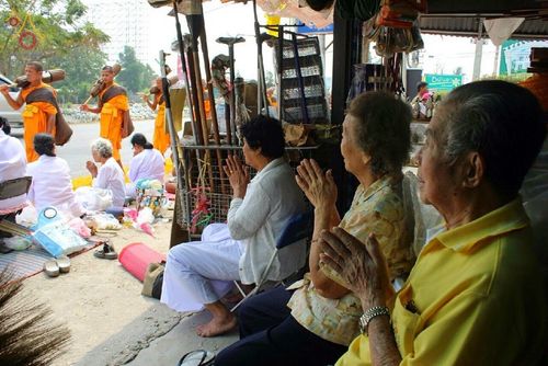 พุทธศาสนิกชนนั่งพนมมือรอต้อนรับคณะพระภิกษุสงฆ์ที่กำลังเดินธุดงค์ผ่านริมถนน