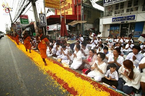 พระภิกษุสงฆ์เดินธุดงค์บนเส้นทางที่ปูด้วยกลีบดอกดาวเรืองท่ามกลางพุทธศาสนิกชนที่นั่งรอต้อนรับ