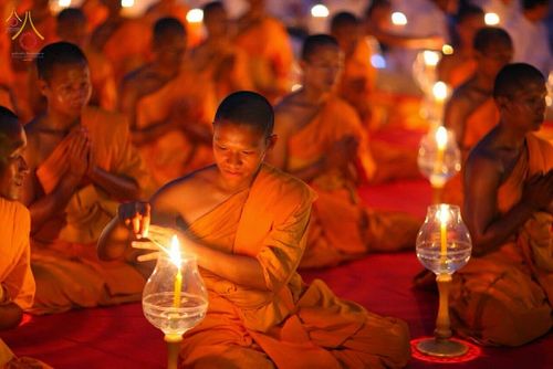 พระภิกษุสงฆ์กำลังจุดเทียนในโคมแก้วท่ามกลางกลุ่มพระสงฆ์ที่นั่งสมาธิในพิธีทางศาสนา