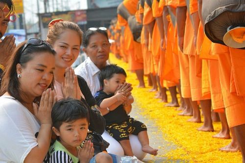 กลุ่มพุทธศาสนิกชนนั่งพนมมือต้อนรับคณะพระธุดงค์ที่เดินผ่านเส้นทางโปรยดอกดาวเรือง