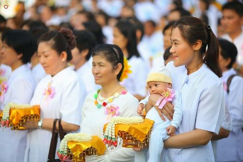 กลุ่มพุทธศาสนิกชนสวมชุดขาวถือพานพุ่มดอกมะลิและหญิงสาวอุ้มทารกเข้าร่วมพิธีกรรมทางศาสนาที่วัดพระธรรมกาย