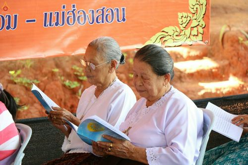 หญิงสูงวัยสองท่านสวมชุดขาวถือหนังสือสวดมนต์ในพิธีทอดกฐิน