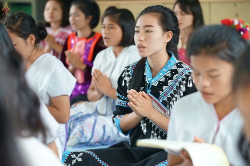 กลุ่มเยาวชนหญิงสวมชุดพื้นเมืองกำลังพนมมือสวดมนต์อย่างตั้งใจในกิจกรรมทางศาสนา
