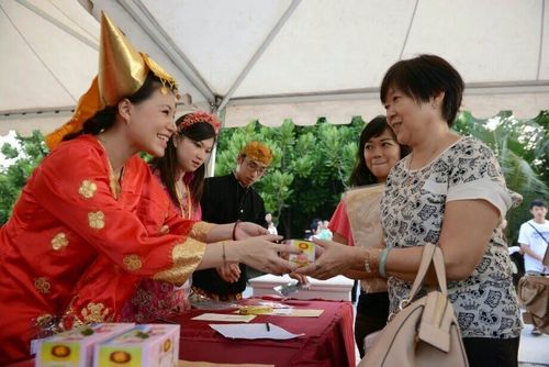 หญิงสาวในชุดสีแดงกำลังส่งมอบกล่องของที่ระลึกให้แก่ผู้ร่วมงานในงานวิสาขบูชาที่ Ancol beach