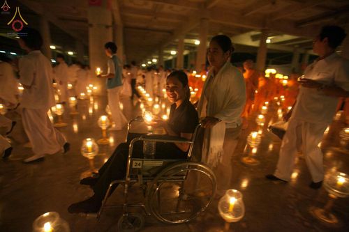 หญิงสาวนั่งรถเข็นถือประทีปท่ามกลางพุทธศาสนิกชนที่มาร่วมจุดประทีปในวันครูผู้ค้นพบวิชชาธรรมกาย