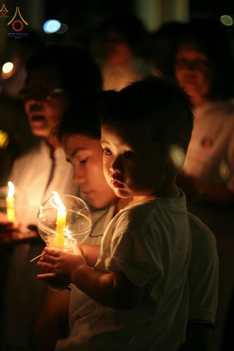 เด็กน้อยถือโคมเทียนแก้วใสร่วมพิธีจุดเทียนในงานศาสนา