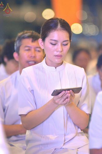 หญิงสาวสวมชุดสีขาวถือโทรศัพท์มือถือด้วยความตั้งใจในงานพิธีกรรมทางศาสนา