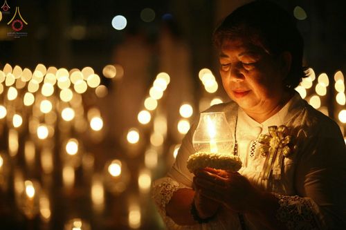 หญิงสวมชุดขาวถือโคมประทีปในพิธีจุดประทีปท่ามกลางแสงไฟสว่างไสว