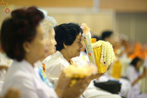 หญิงสูงวัยสวมชุดขาวถือพานดอกไม้และหนังสือในพิธีทางศาสนา