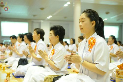 กลุ่มพุทธศาสนิกชนสวมชุดขาวนั่งสมาธิและพนมมือด้วยความสงบภายในอาคาร เพื่อร่วมกิจกรรมเนื่องในวันครูผู้ค้นพบวิชชาธรรมกาย