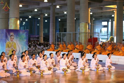 กลุ่มพุทธศาสนิกชนในชุดขาวนั่งพนมมือปฏิบัติธรรมร่วมกับคณะสงฆ์ภายในอาคารกว้างขวาง