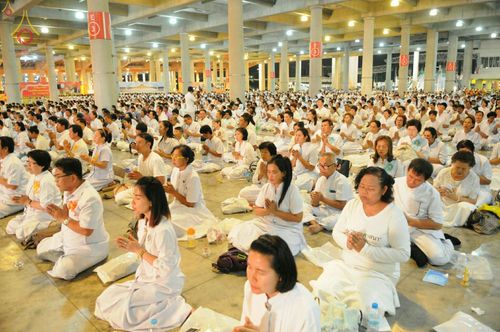 กลุ่มพุทธศาสนิกชนสวมชุดขาวนั่งสมาธิปฏิบัติธรรมร่วมกันภายในอาคารขนาดใหญ่