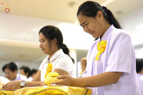 หญิงไทยสวมชุดสีขาวกำลังประกอบพิธีกรรมทางศาสนาด้วยความตั้งใจและมีรอยยิ้ม