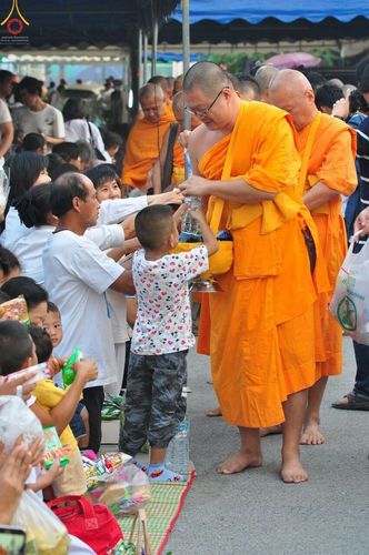 พระภิกษุรับบิณฑบาตน้ำดื่มจากเด็กชายและพุทธศาสนิกชนในกิจกรรมตักบาตรที่วัดพระธรรมกาย